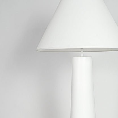 Close view of table lamp with white shade and minimal base design showcasing clean contemporary lighting style on neutral background.