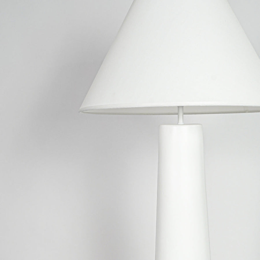 Close view of table lamp with white shade and minimal base design showcasing clean contemporary lighting style on neutral background.