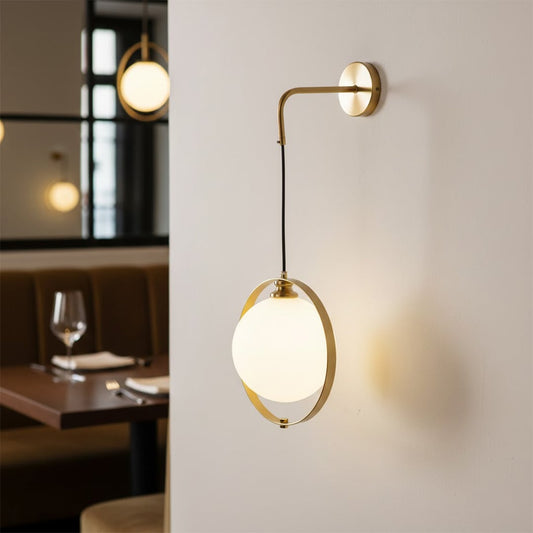 Elegant gold wall fixture with a suspended frosted glass globe orb casting a soft warm glow in a luxury restaurant space.
