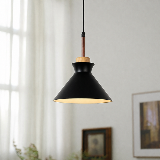 A modern pendant light with a matte black conical shade, a warm yellow LED light glowing from within, a natural wood accent ring, and a copper-colored metal rod, hanging in a softly lit room with white curtains.