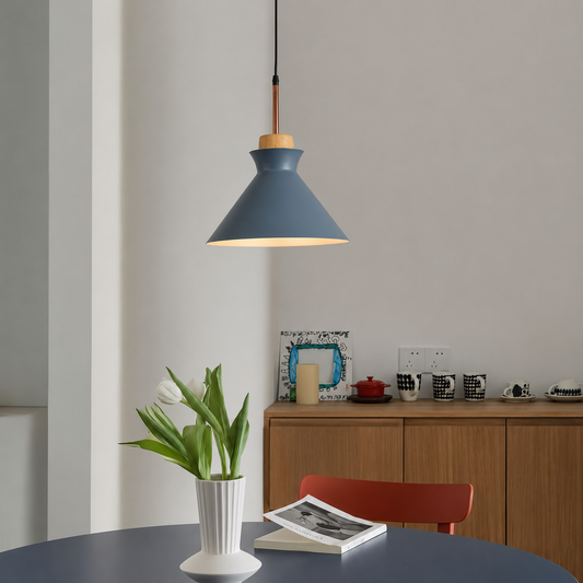 A modern pendant light with a slate blue conical shade, a light wood top, and a black cord hanging over a dining table in a minimalist room.