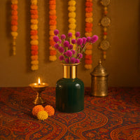 Dark green ceramic vase with a gold rim filled with pink flowers styled beautifully for festive home decor with marigold garlands in the background.