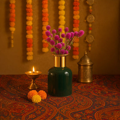 Dark green ceramic vase with a gold rim filled with pink flowers styled beautifully for festive home decor with marigold garlands in the background.