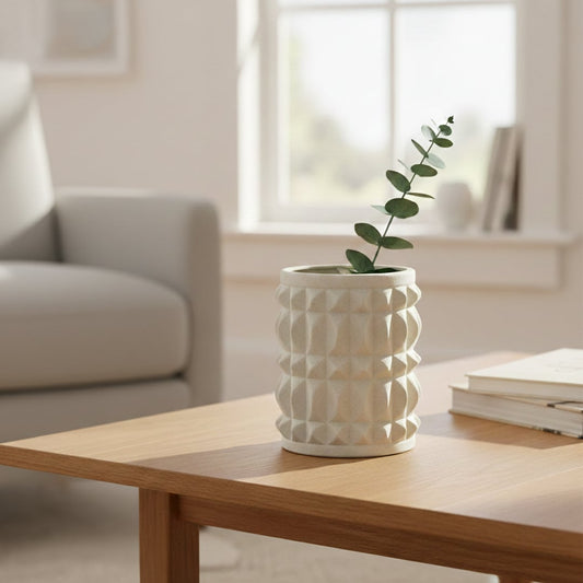 Light beige textured ceramic decorative planter styled with green stem on wooden coffee table in bright modern living room.