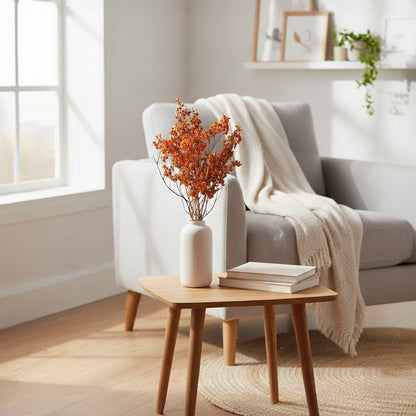 Bright orange preserved dollar eucalyptus branches in a white vase on a side table next to a cozy living room armchair.