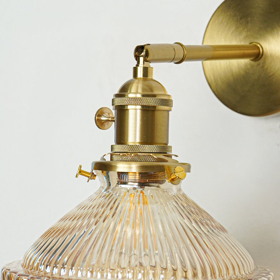 Closeup of gold metal wall light with ribbed glass shade showcasing intricate detailing and premium finish for modern decor styling.