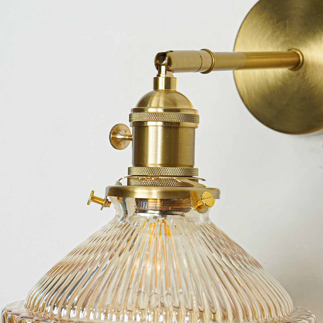 Closeup of gold metal wall light with ribbed glass shade showcasing intricate detailing and premium finish for modern decor styling.