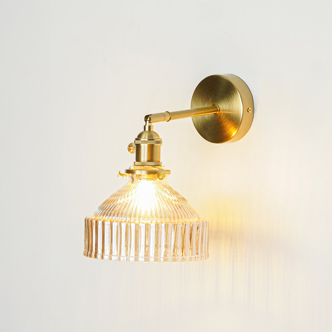 Gold metal wall light with ribbed glass shade emitting warm glow ideal for modern bathroom or bedroom wall decor placement.