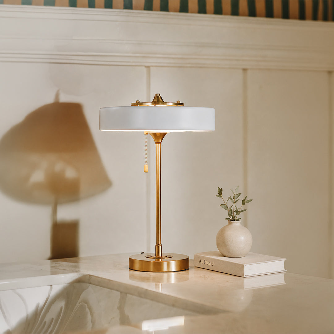 White glass table lamp with brass metal base placed on a side table creating elegant contemporary ambient lighting.