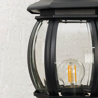 Detailed zoom view of black outdoor pillar lamp with curved transparent glass panels highlighting glowing LED bulb.