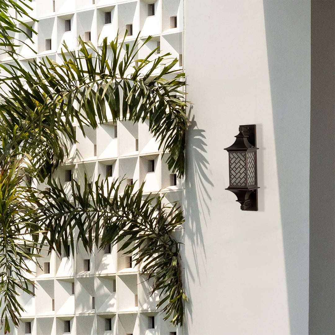 Modern bronze outdoor column wall light lifestyle image with basketweave lattice overlay on a white villa wall with palms.