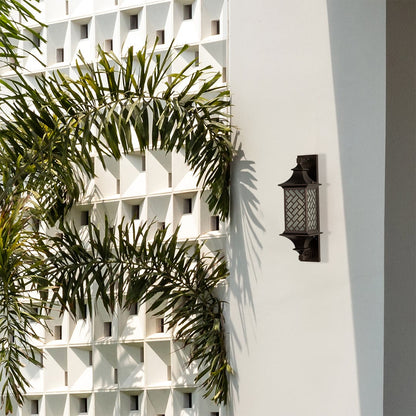 Modern bronze outdoor column wall light lifestyle image with basketweave lattice overlay on a white villa wall with palms.