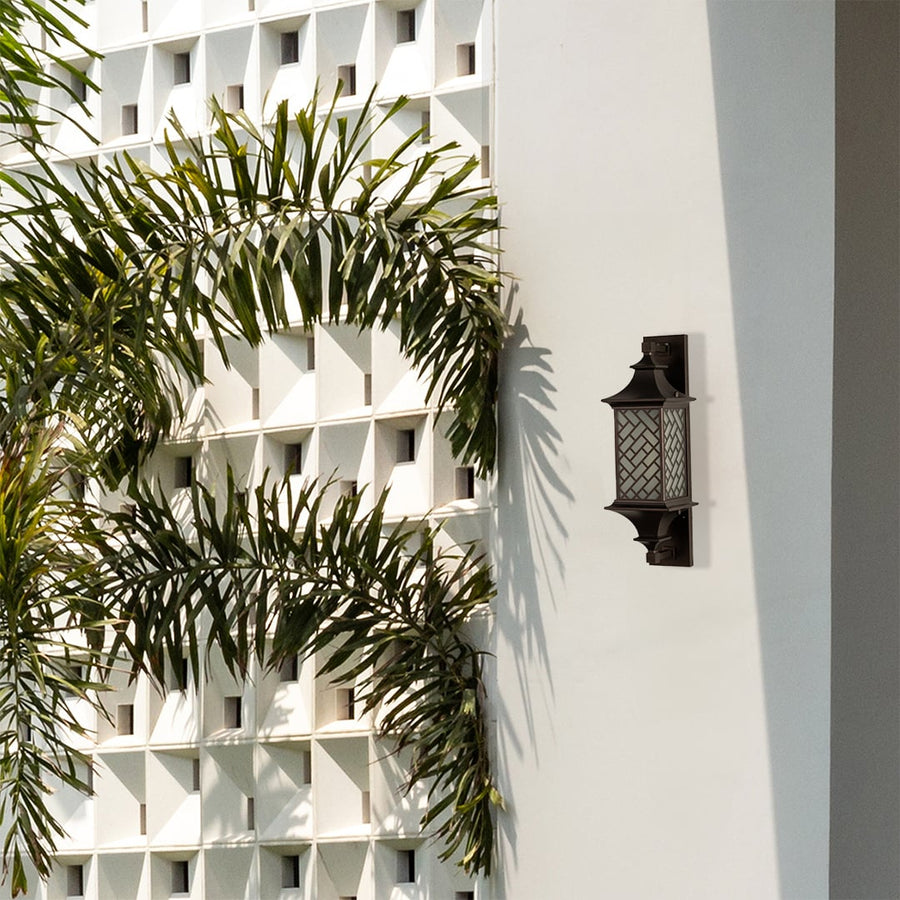 Modern bronze outdoor column wall light lifestyle image with basketweave lattice overlay on a white villa wall with palms.