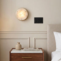 Round white marble flush mount wall sconce light above wood nightstand bed for minimalist bedroom home decor styling.