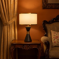 Black ceramic table lamp with golden accents and fabric drum shade adding warm lighting to classic living room decor.