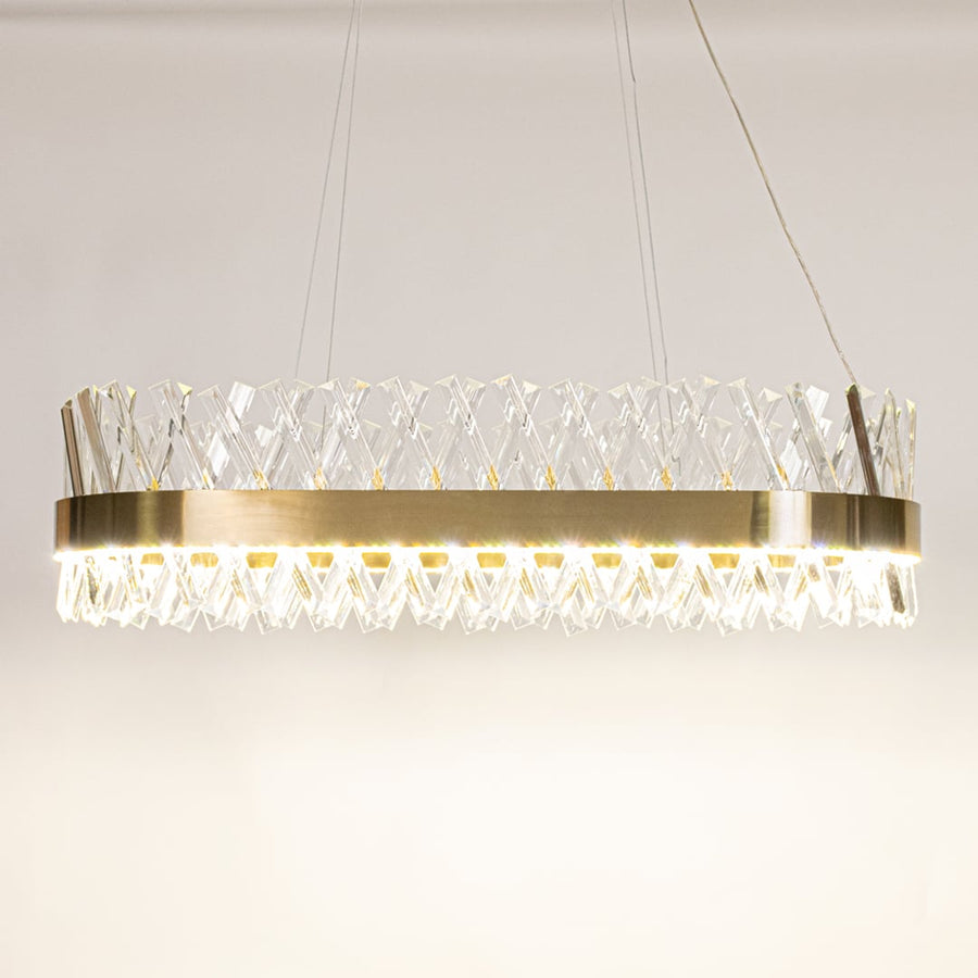 Gold metal chandelier with clear crystal rods shown with lights on against a white background highlighting its glowing sophisticated illumination.