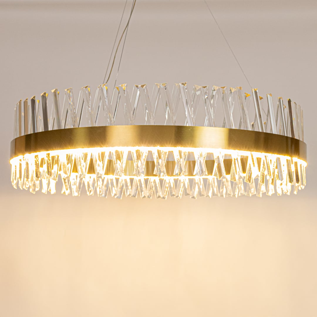 Gold metal chandelier with crystal rods displayed with lights on highlighting its clean round silhouette and premium glass texture.