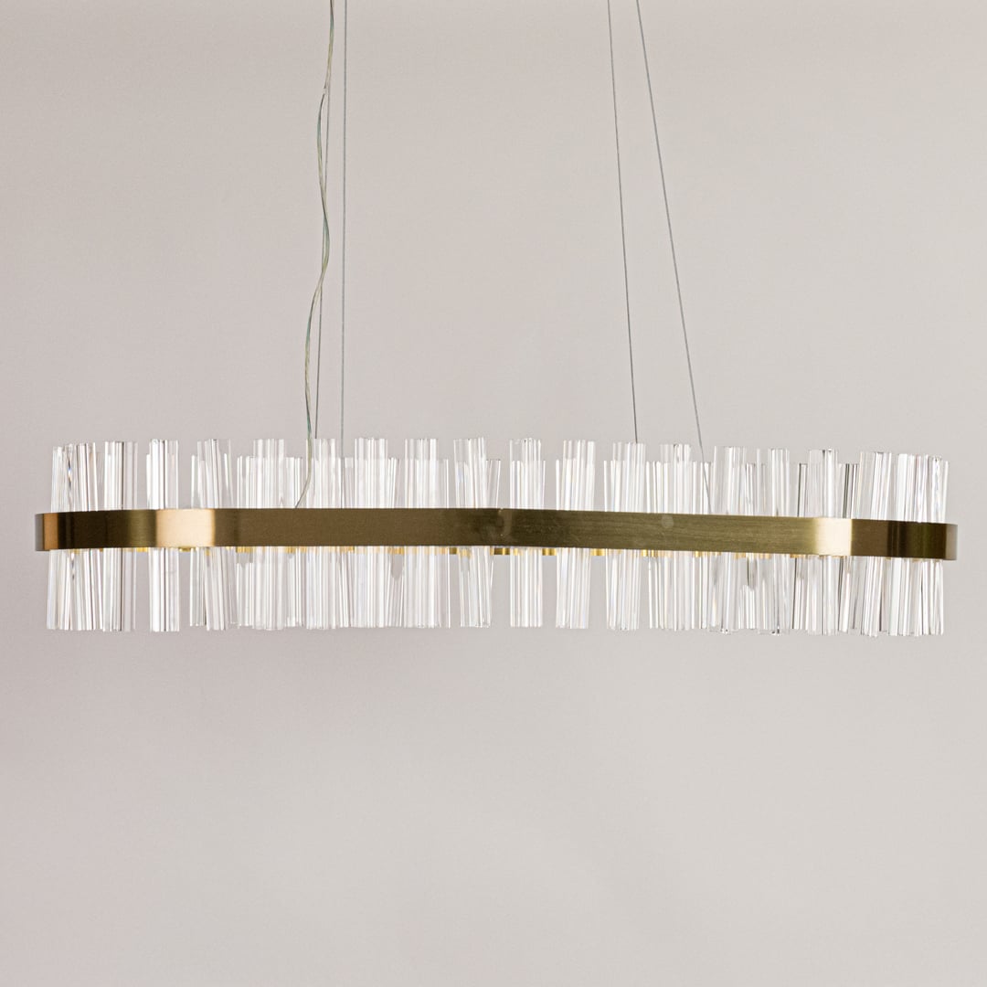Gold metal chandelier with clear crystal rods displayed with lights off on a clean white background showcasing its sleek elongated shape.