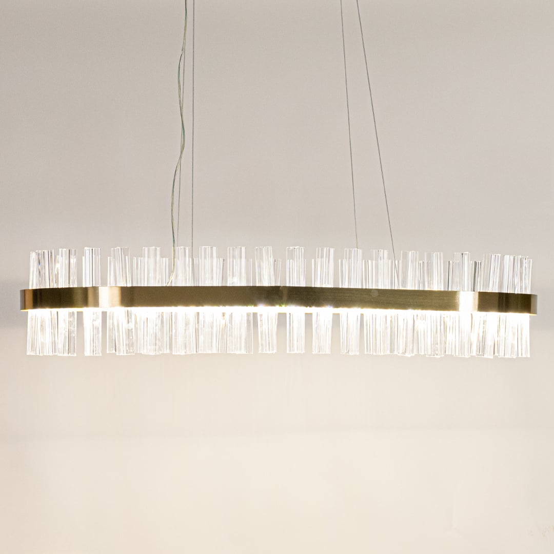 Gold metal chandelier with crystal rods shown with lights on creating a warm luxurious glow for modern interior spaces.