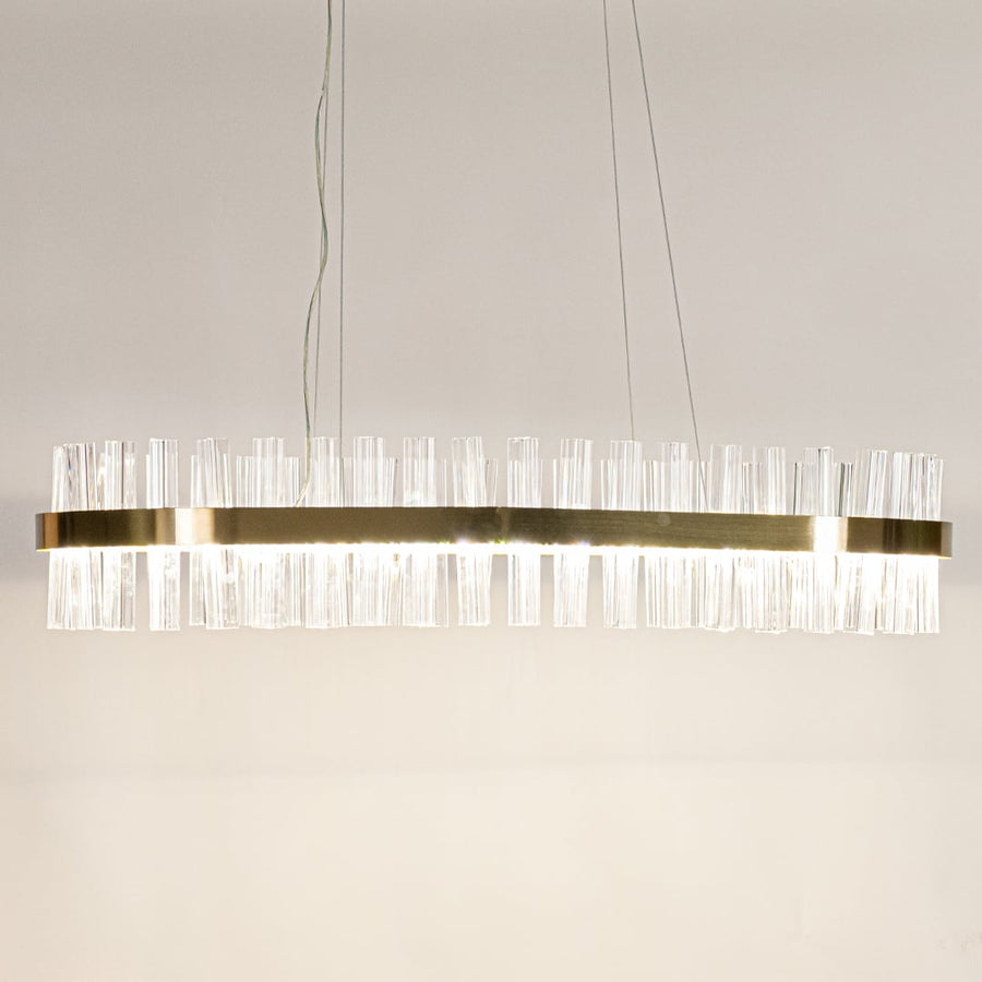 Gold metal chandelier with crystal rods shown with lights on creating a warm luxurious glow for modern interior spaces.