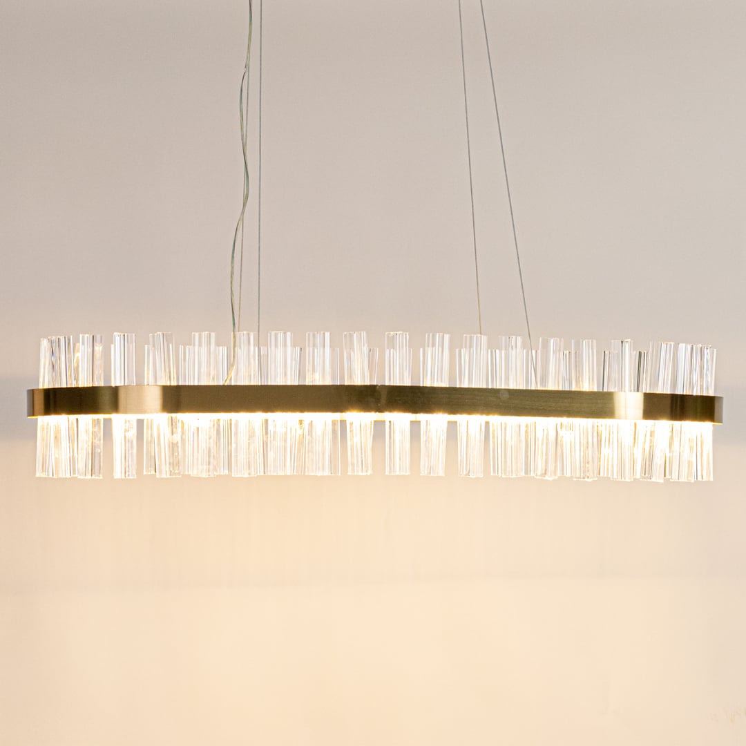 Gold metal chandelier with clear crystal rods displayed with lights on highlighting its sleek modern elongated frame.