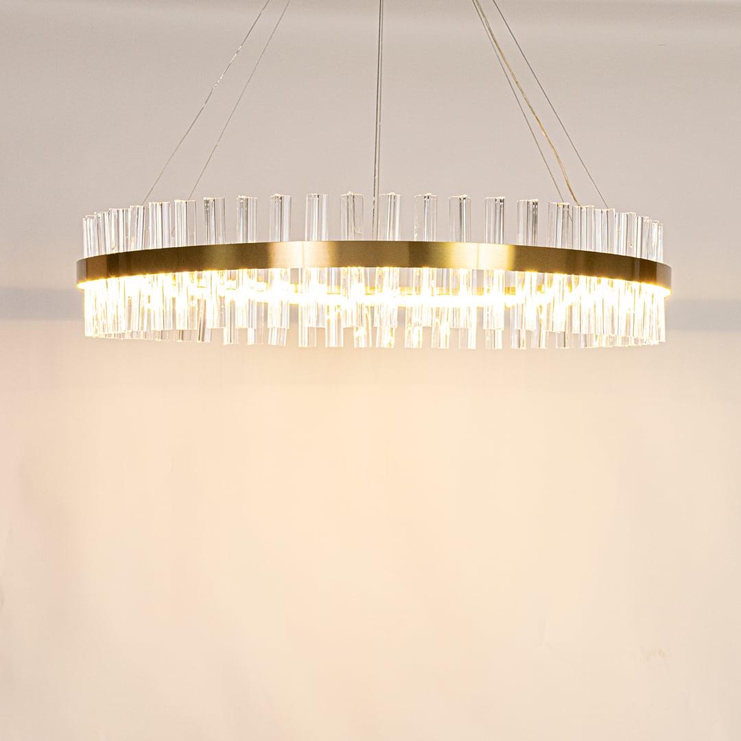 Gold metal chandelier with crystal rods shown with lights on creating a warm elegant and sparkling lighting effect.