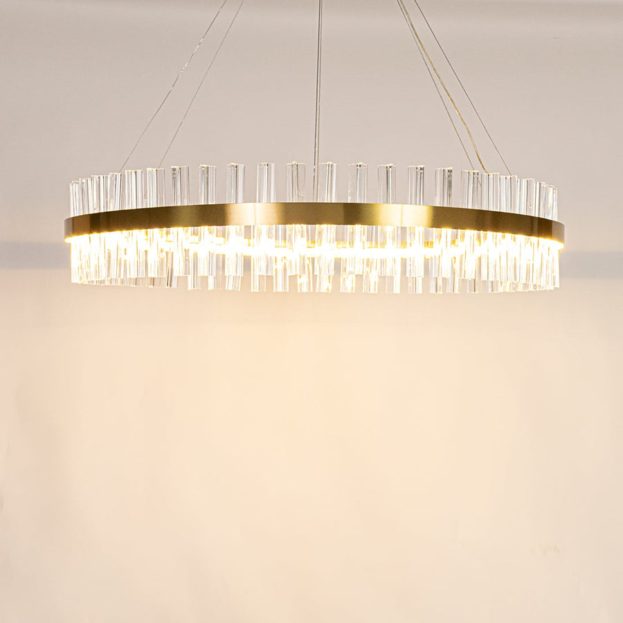 Gold metal chandelier with crystal rods shown with lights on creating a warm elegant and sparkling lighting effect.