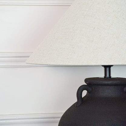 Closeup of black ceramic table lamp showing matte textured surface sculpted handles and fabric shade with clean detailing.