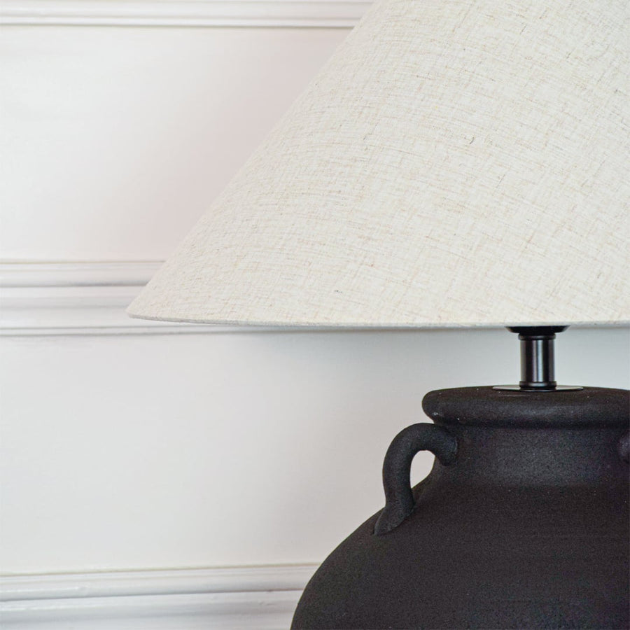 Closeup of black ceramic table lamp showing matte textured surface sculpted handles and fabric shade with clean detailing.