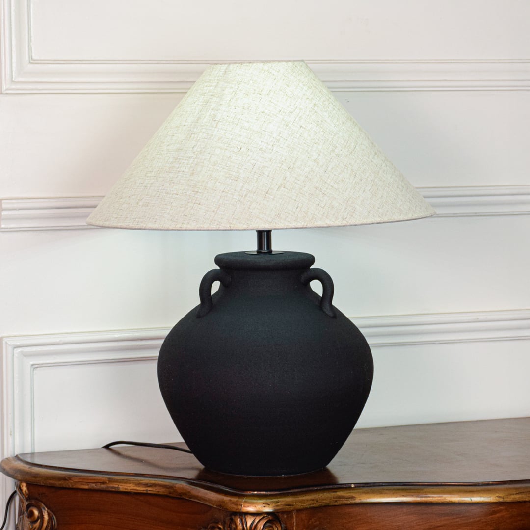 Black ceramic table lamp featuring textured matte finish rounded pot base and wide fabric shade displayed on white background.