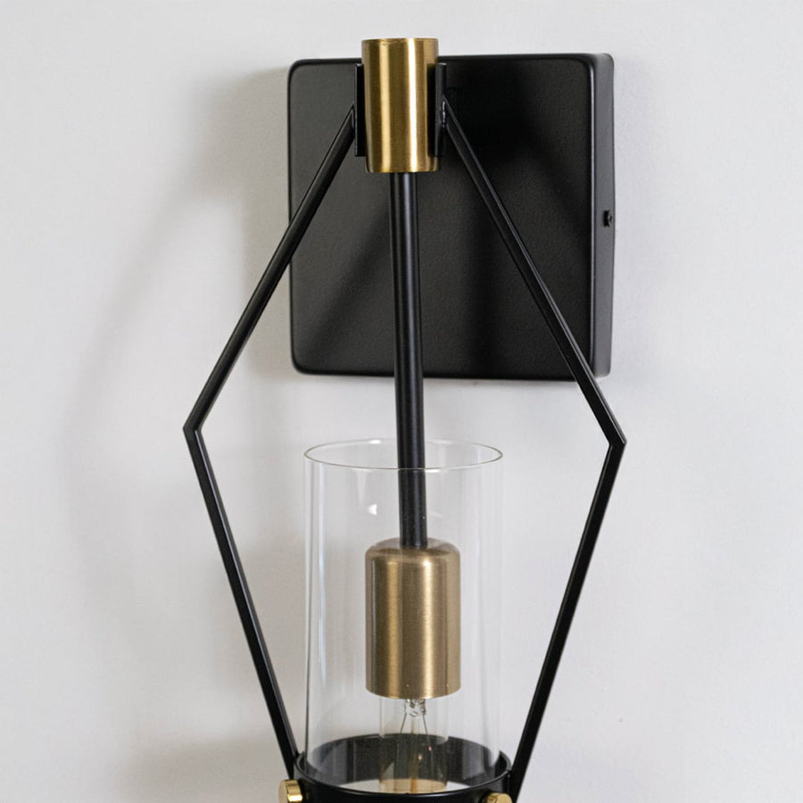 Closeup of black metal wall sconce with gold details and clear glass tube shade highlighting premium modern finish.
