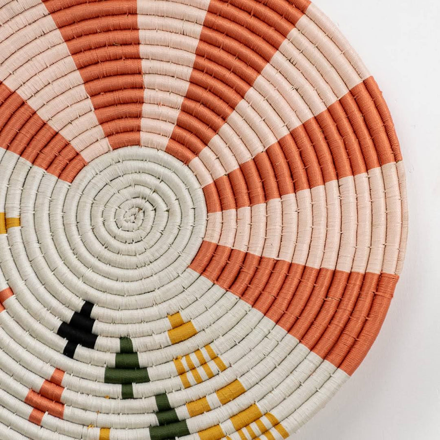 Closeup of handcrafted seagrass wall basket with coral orange cream and black spiral woven pattern for artisan home décor.