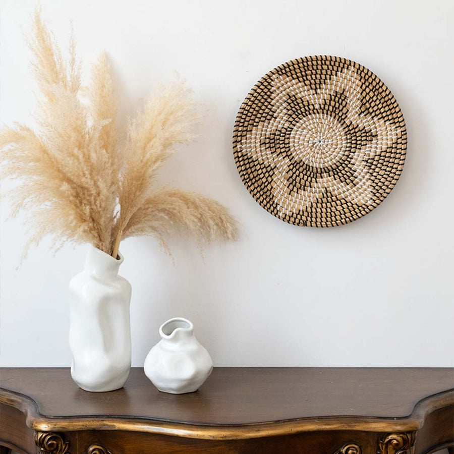 Handwoven wicker basket wall decor styled with pampas grass in vase on wooden console for modern boho home interiors.