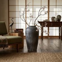 Black textured floor vase with dried branches placed indoors for rustic modern home decor styling.