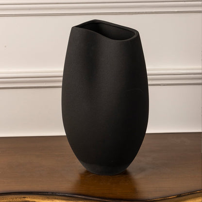 Matte black ceramic vase with sleek oval form and asymmetrical rim on white background showcasing modern artistic design.