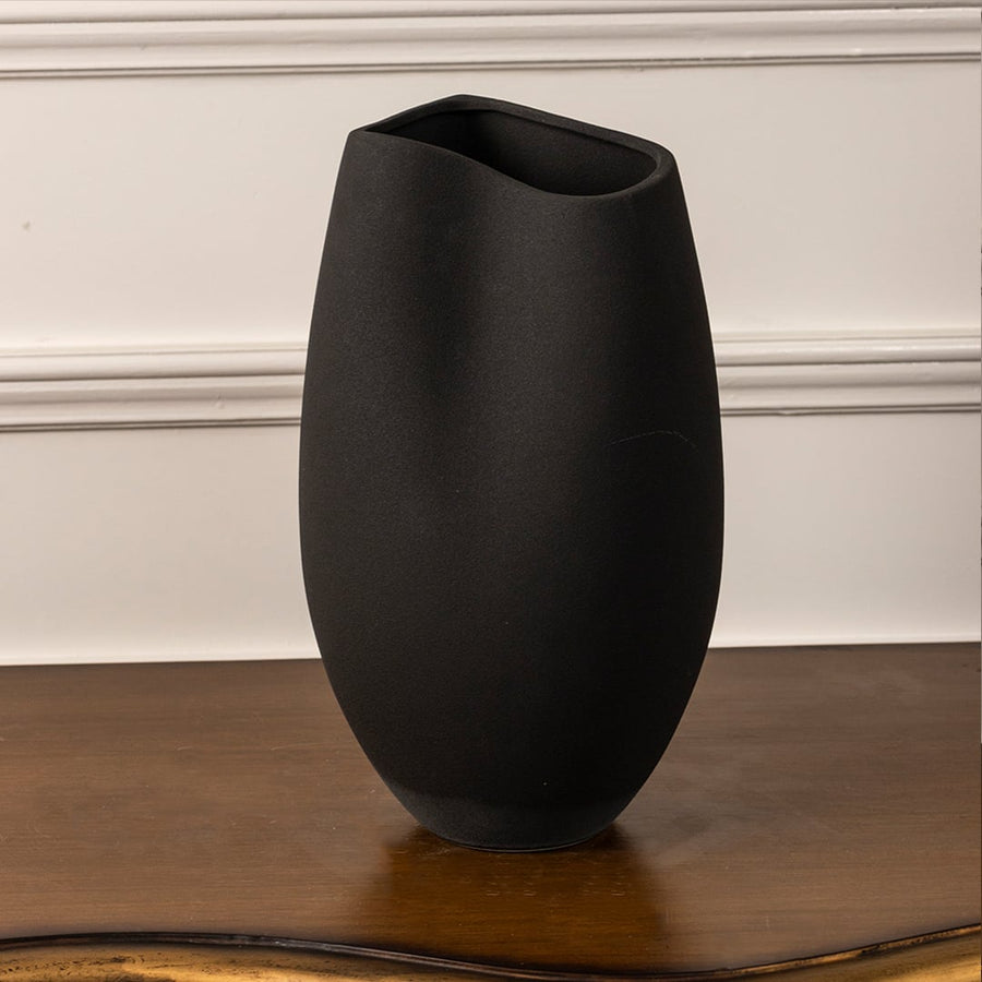 Matte black ceramic vase with sleek oval form and asymmetrical rim on white background showcasing modern artistic design.