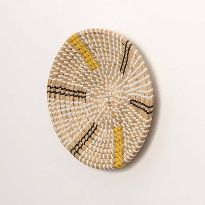 Side view of handcrafted natural cream seagrass wall basket with yellow and black striped spokes for boho wall decor.