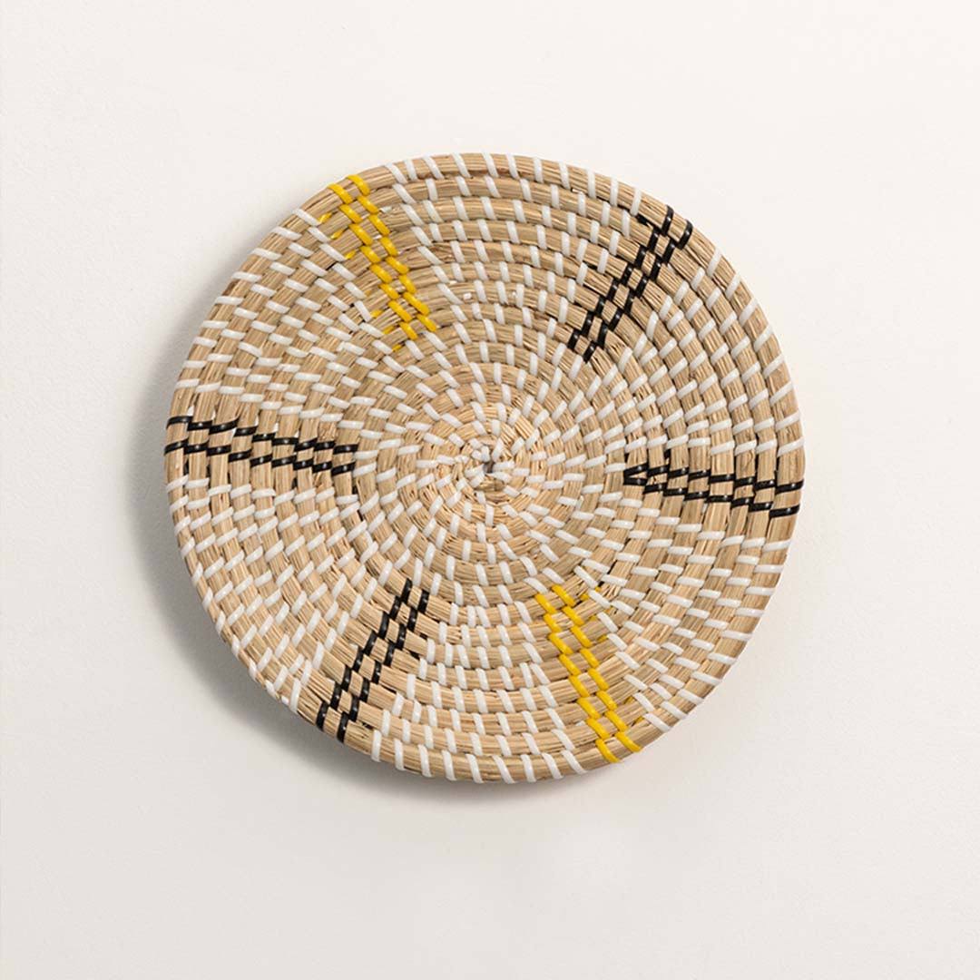 Round handcrafted natural cream seagrass wall basket with yellow and black radial spoke patterns on white background.