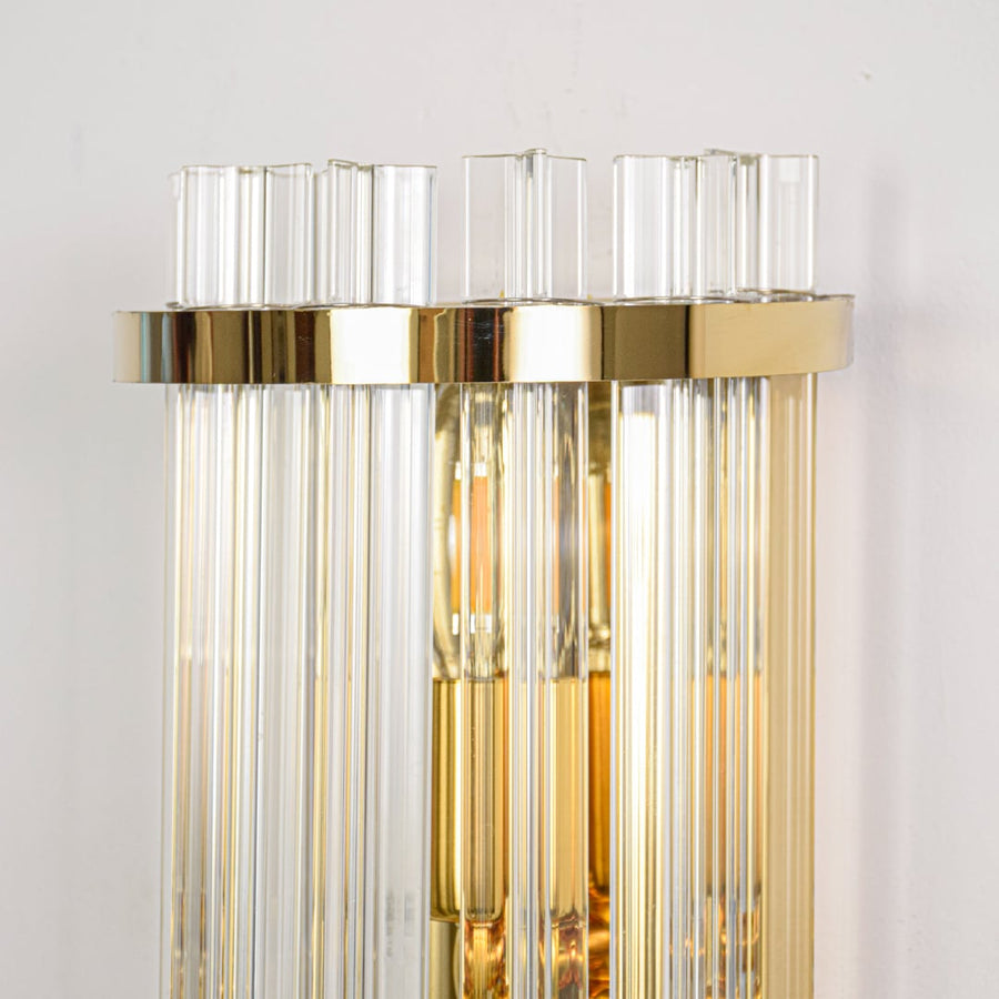 Closeup of gold metal wall light highlighting clear vertical glass rods polished finish and refined modern craftsmanship.