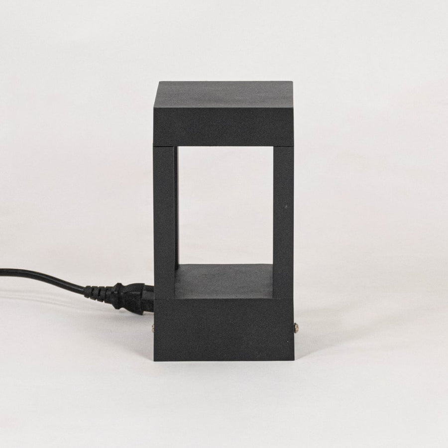 Minimal black pillar light with matte metal frame displayed off on plain white background surface.