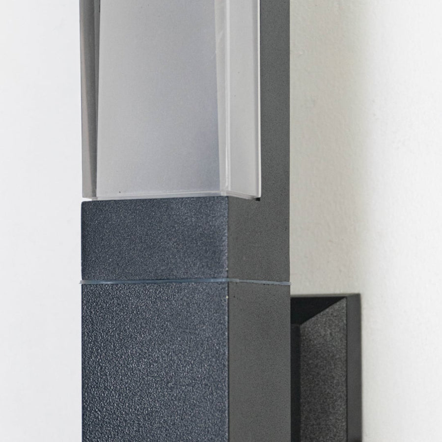 Closeup of modern outdoor wall light showing rectangular metal body frosted diffuser and durable weather resistant finish.