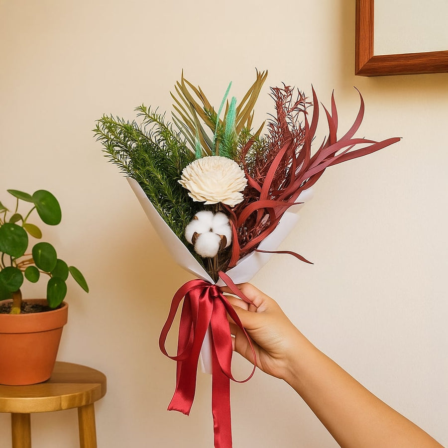 Lifestyle image showing preserved dried flower bouquet wrapped in white paper with red ribbon held by hand enhancing modern home decor.