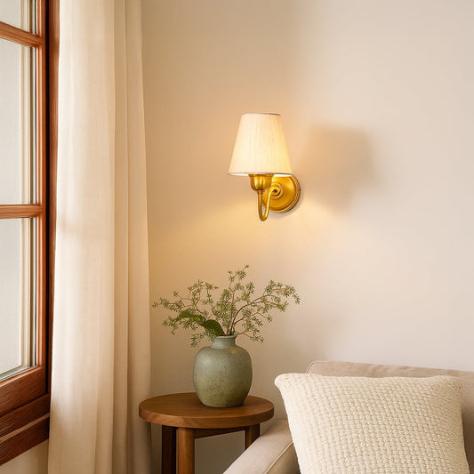 Classic brass wall sconce with white fabric shade and curved arm mounted on wall creating timeless home interior lighting.