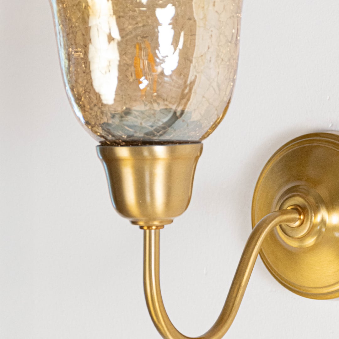 Detailed close up of brass wall light showing smooth curved arm polished metal finish and textured amber glass construction.