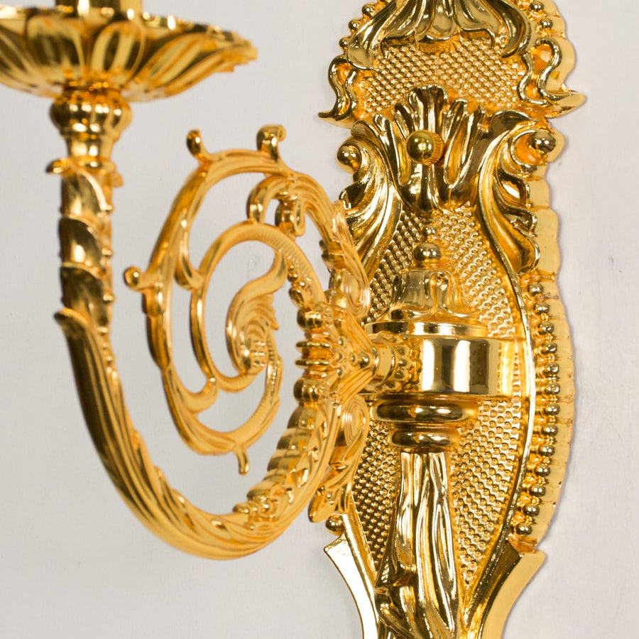 Closeup of gold wall light showing intricate carved detailing and candle style bulb for premium interior lighting design.
