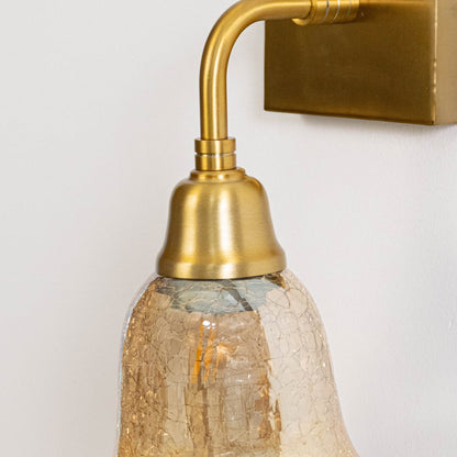 Closeup of gold metal wall light showing curved arm textured glass shade and warm bulb glow with refined vintage detailing.
