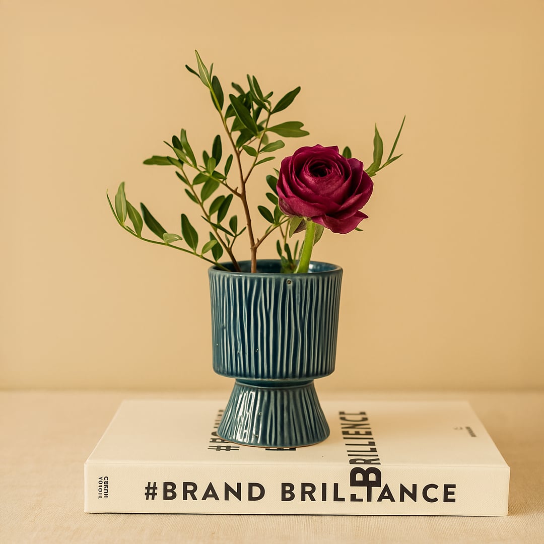 Elegant blue textured vase with a deep red rose and green foliage placed on a Brand Brilliance book creating a refined modern decor look.