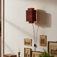 Wooden wall light with vertical slatted shade casting warm ambient glow on white wall styled with vintage frames plants and decor accents.