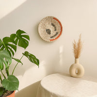Handmade circular wall decor in natural fiber finish mounted near indoor plants adding organic texture and relaxed home styling.