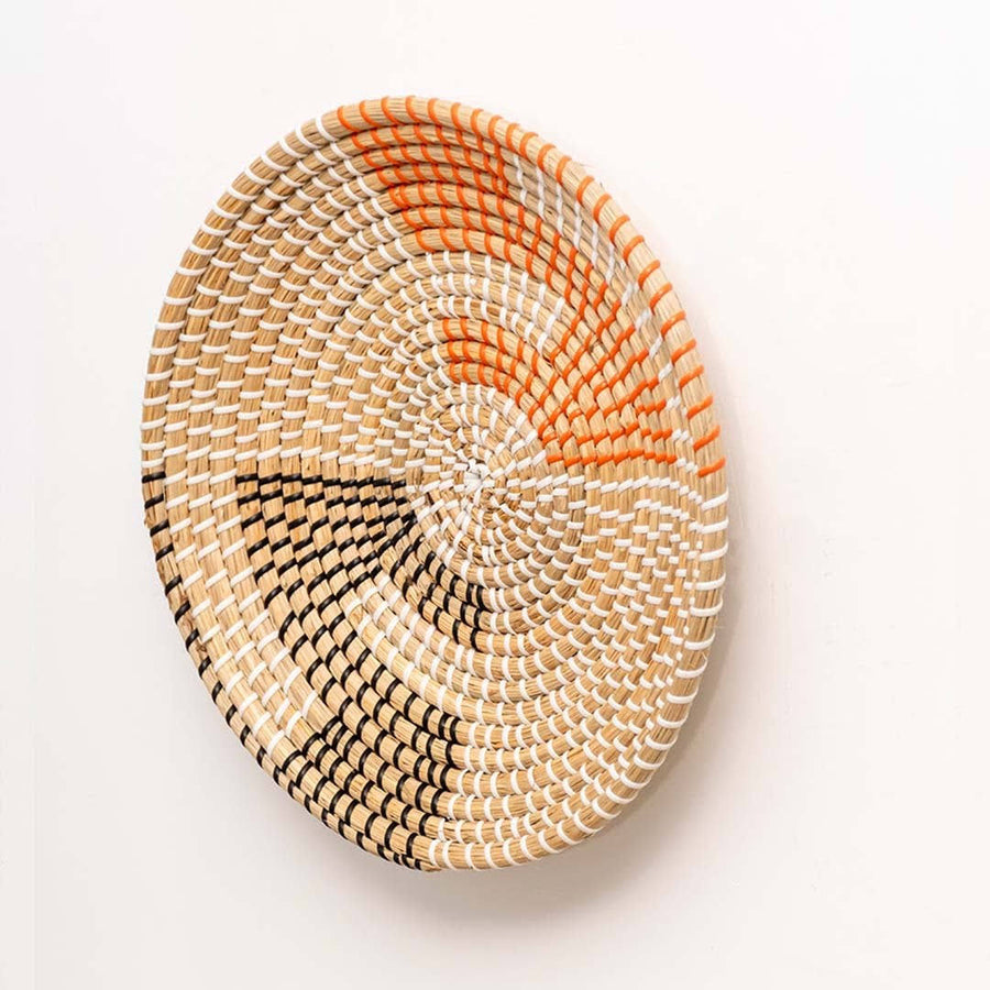 Side view of round handwoven seagrass basket with orange and black weave details for living room wall art decor display.